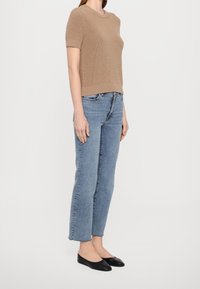 Beige stickad kortärmad tröja i kombination med ljusblå raka jeans och svarta platta skor. Enkel, ren design utan mönster.