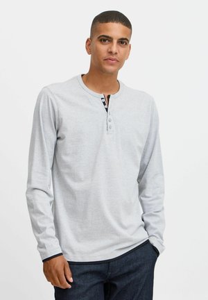 Siva dugmadna henley majica s dugim rukavima, izrađena od mekog materijala, koja ima placket sa dugmadi s crnim akcentima i kontrastnim manžetama rukava.