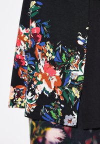 Schwarzes Kleidungsstück mit einem bunten Blumenmuster in Rot, Orange, Gelb und Blau. Der Stoff wirkt weich und hat eine glatte Textur.