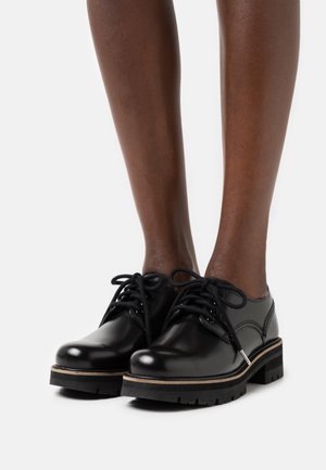 Chaussures en cuir noir à lacets avec une finition lisse, présentant une semelle épaisse et une bande contrastante plus claire le long du bord.