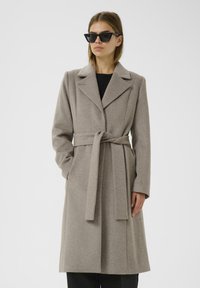 Cappotto di lana grigio chiaro con cintura, revers a punta, tasche laterali e maniche lunghe, caratterizzato da una texture liscia e un design sartoriale.