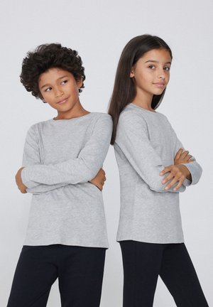 Deux enfants portent des chemises en coton à manches longues de couleur gris clair, se tenant dos à dos avec les bras croisés, sur un fond uni.