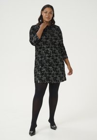 Robe noire à sequins avec des manches courtes et une coupe ample. Assortie à des collants noirs et des escarpins à bout pointu avec des accents en argent.