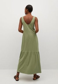 Pitkään, hihattomaan mekkoon on käytetty pehmeää oliivinvihreää kangasta. Mekossa on V-muotoinen selkäosa, kerroksellinen helma ja sileä tekstuuri, ja se on yhdistetty mustiin remmisandaaleihin.