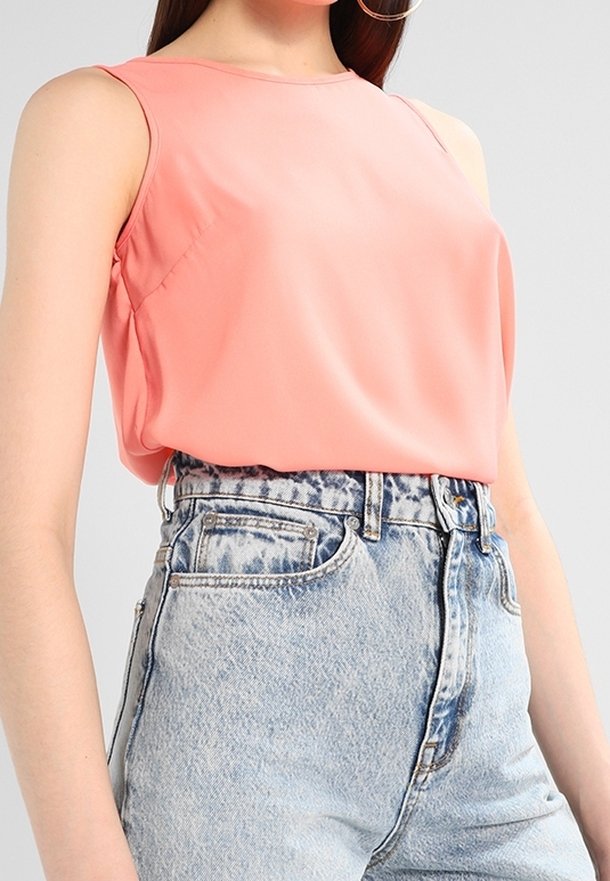 Růžová halenka bez rukávů v kombinaci s džínami s vysokým pasem a světlou acid-wash úpravou na osobě před neutrálním pozadím.