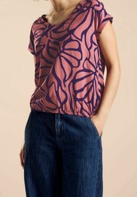 Short-sleeve top in pink with a dark purple floral pattern; flowy material and a gathered hem, paired with dark denim wide-leg pants.