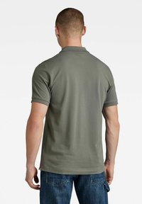 Olijfgroene polo met korte mouwen, gemaakt van gladde stof. Heeft een klassieke kraag en een rechte zoom, gecombineerd met donkerblauwe jeans.