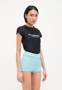 Schwarzes Kurzarm-Rashguard mit weißem "BILLABONG AUSTRALIEN"-Logo, kombiniert mit hellblauen, strukturierten, hoch geschnittenen Shorts.