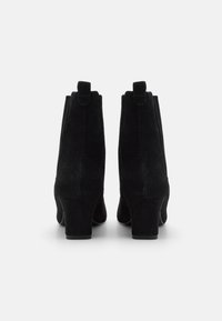 Botines de ante negro con puntera redonda, tacón bajo cuadrado y tiradores en la parte trasera para ponérselos fácilmente. Textura suave y mate.