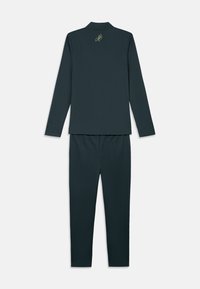 Σκούρο τιρκουάζ μπλούζα με μακριά μανίκια και αντίστοιχες παντελόνες τοποθετημένα επίπεδα, η μπλούζα έχει ένα μικρό κίτρινο κεντητό λογότυπο κοντά στην γραμμή του λαιμού στο πίσω μέρος.