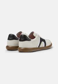 Un paio di sneaker crema con tacco e accenti laterali neri, bordi bianchi e suole marroni su uno sfondo bianco uniforme.