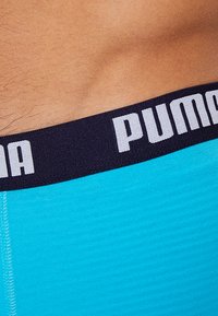 Turquoise boxer briefs with a black elastic waistband featuring the white "PUMA" logo, showcasing a smooth texture and fitted design.