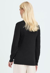 Schwarzer Strickpullover mit langen Ärmeln und gerippten Bündchen, mit lockerer Passform und glatter Textur, von hinten präsentiert.