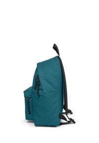 Mochila de tela color verde azulado con una solapa redondeada, correas ajustables, un bolsillo lateral y detalles en negro. Textura suave con detalles de cordón.