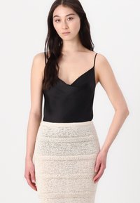 Camisole en satin noir avec des fines bretelles, associé à une jupe en tricot crème comportant des rayures texturées horizontales.