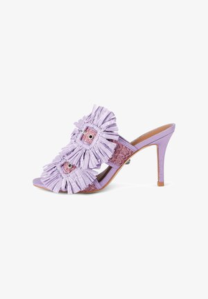 Mule lilas à talon haut avec bout ouvert, deux brides décoratives à franges avec œillets en métal, et détail de semelle intérieure tissée texturée.