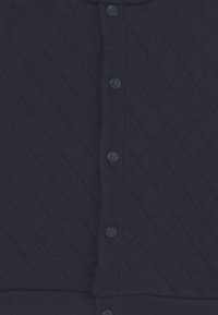 Marinblå quiltad tyg med diamantmönster och en rad av fem matchande tryckknappar i mitten.