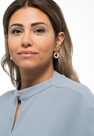 Haut bleu clair avec un col mandarin. Boucles d'oreilles en or en forme de créole avec des grappes de perles blanches. Texture lisse ; cheveux jusqu'aux épaules.