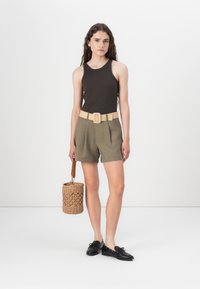 Tamsiai rudas triko, šviesiai alyvuogių žaliai šortai su raukšlėmis, bežė pintas diržas, juodi batai ir apvalus pintas krepšys su rankena.