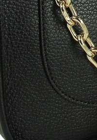 Zwarte leren handtas met een getextureerde afwerking, een gebogen vorm en een gouden metalen kettingriem voor extra hardwaredetail.