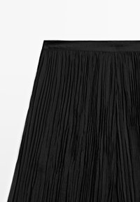 Black pleated skirt with a smooth waistband, textured fabric, and vertical pleats creating a layered effect.