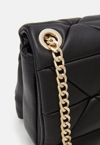 Sac à main noir en cuir matelassé avec une bandoulière en chaîne dorée et des détails en érable doré ronds. Surface texturée avec des sections rembourrées.