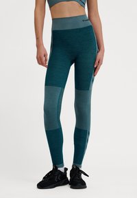 Leggings realizzati in tessuto teal con diverse trame, pannelli in rete e una vita alta. Includono un dettaglio con logo sulla vita.
