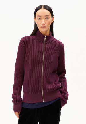 Lila gerippter Strickzipper mit hohem Kragen und silbernem Reißverschluss. Das Kleidungsstück hat lange Ärmel und einen taillierten Saum.