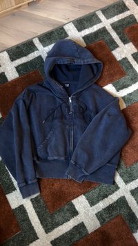 Marineblaue Kapuzenjacke mit Reißverschluss aus weichem Stoff, ausgestattet mit einer Fronttasche, einer Kapuze mit Kordelzug und dem gestickten "GAP"-Logo auf der Brust.