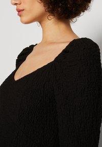 Svart texturerad klänning med djup V-ringning och puffärmar. Tyget har ett veckat mönster för extra dimension.