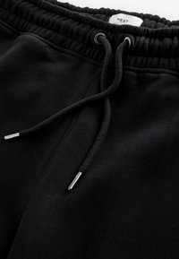 Pantalones de chándal negros con cintura elástica y cordón ajustable. La tela parece suave con una textura lisa. Presenta aglets plateados.