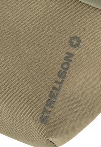 Borsetta in tessuto verde oliva con superficie testurizzata e logo "STRELLSON" in rilievo di colore grigio scuro, che evidenzia il suo design semplice e il materiale.
