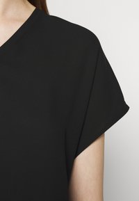 Haut noir à manches courtes avec une coupe décontractée, présentant un col en V et une texture lisse. Le tissu a une finition mate et un drapé subtil.