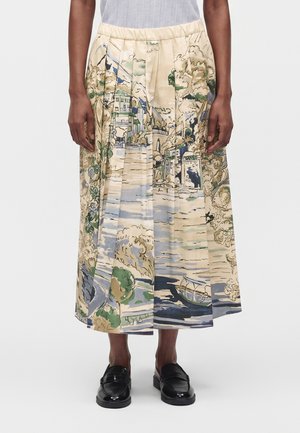 Jupe midi plissée avec un imprimé pittoresque d'arbres, d'eau, de maisons et d'un bateau, portée avec des mocassins noirs et un haut clair.