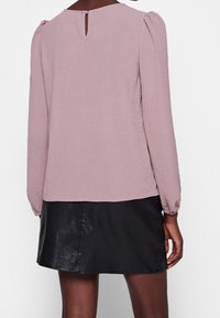 Haut à manches longues rose clair avec tissu texturé, fermeture au dos en forme de goutte d'eau ; associé à une mini-jupe en cuir noir.