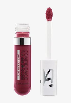 Tube de gloss à lèvres étiqueté « Confidence In A Serum Gloss 90 % Hydration Base », avec l'applicateur montrant un gloss rose sur un fond blanc.