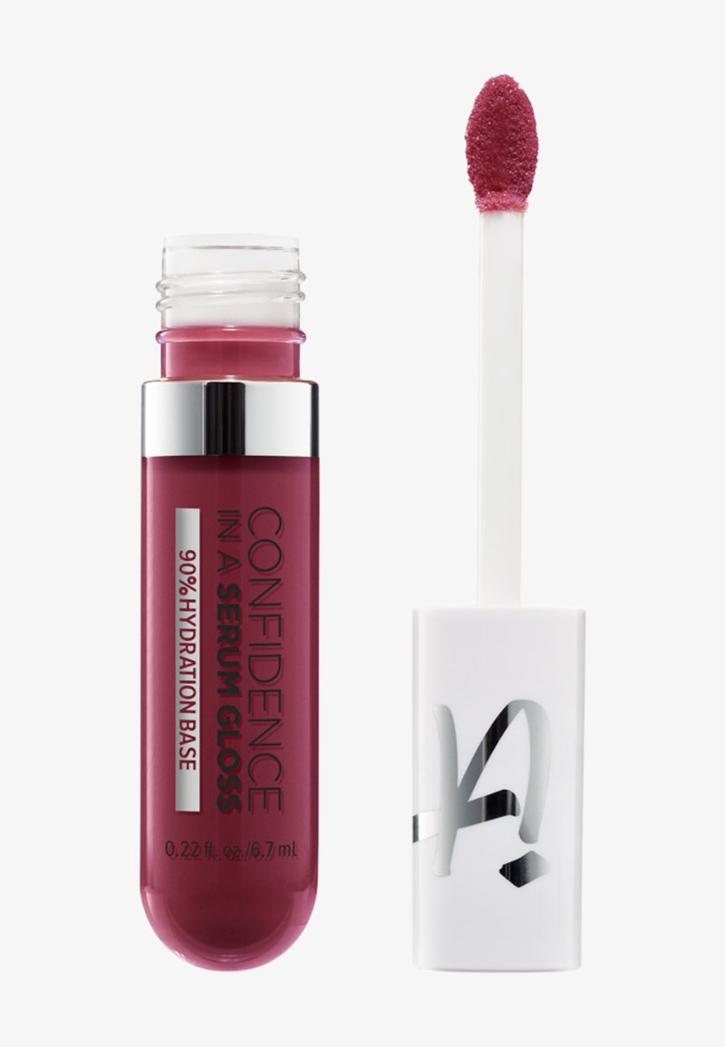 Tube de gloss à lèvres étiqueté « Confidence In A Serum Gloss 90 % Hydration Base », avec l'applicateur montrant un gloss rose sur un fond blanc.