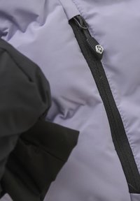 Lila vadderad jacka med svart dragkedja och dragflik. Texturerad yta med sömnadsdetaljer; elastiska muddar är synliga.