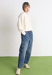 Kreemikas särk, laiad sinised denim püksid ja hallid tossud. Särgil on ümmargune kaelus; püksid on sirge lõikega ja nähtavate õmblustega.