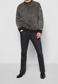 Donkergrijze, gestructureerde sweatshirt met een ronde hals en geribde manchetten, gecombineerd met donkere jeans en zwarte chunky hakken.