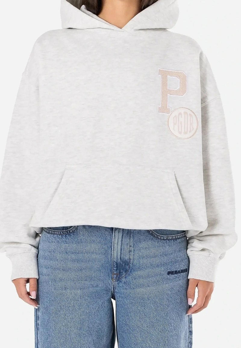 Sweat à capuche gris clair avec grande poche avant, poignets côtelés et logos beige "P" et "PGDR" sur la partie supérieure gauche de la poitrine, porté avec un jean bleu.
