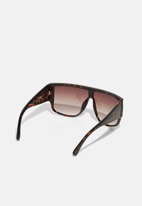 Gafas de sol de carey con montura cuadrada, lentes marrón degradado y varillas delgadas que presentan un patrón de manchas naranjas.