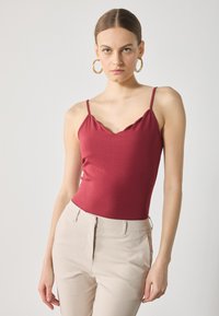 Burgunderfarget bodycon tank topp med bølget hals og tynne stropper,Parret med lyse beige skreddersydde bukser. Glatt stofftekstur.