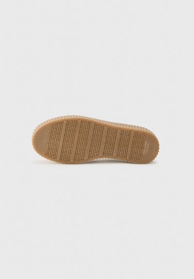 Semelle en caoutchouc de couleur beige avec des rainures horizontales et verticales, présentant une surface texturée et des bords festonnés pour une meilleure adhérence et flexibilité.