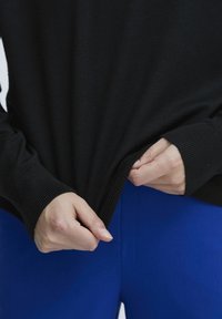 Fekete pulóver bordás ujjak és szegély, ami enyhén meg van húzva, élénk kék nadrággal párosítva. Kiemelkedő textúra és színkontraszt.