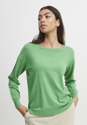 Maglione verde lavorato a maglia con una vestibilità comoda, scollo rotondo e maniche lunghe; texture morbida e polsini e orlo a coste; abbinato a pantaloni beige.