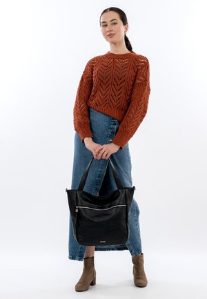 Woman wearing rust knit sweater, blue buttoned denim skirt, and tan ankle boots, holding large black leather tote bag with zipper pocket.