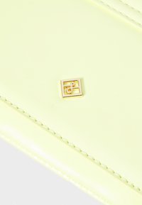 Gelbes Lederportemonnaie mit einem Logo-Akzent in Goldoptik. Die Oberfläche ist glatt, mit genähten Details entlang der Kanten.