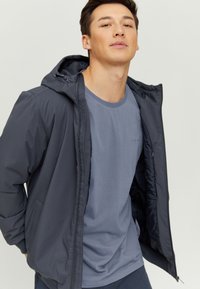 Dark gray zip-up jacket with a hood, featuring a smooth texture and elastic cuffs, layered over a light gray t-shirt with a round neckline.
