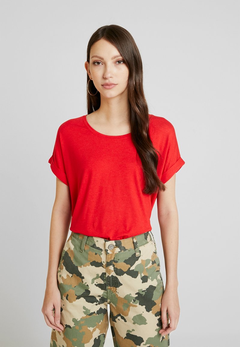 Rotes Kurzarm-T-Shirt mit Rundhalsausschnitt und umgeschlagenen Ärmeln, kombiniert mit camouflagemusterter Hose in Grün- und Beigetönen.